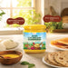 A jar of A2 Gir Cow Desi Ghee is displayed on a kitchen counter surrounded by food props like flatbread, dosas, and a bowl of yellow ghee, with two brown callout bubbles highlighting product benefits.